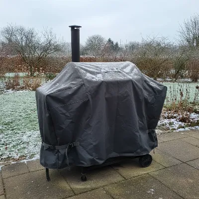 A heavy-duty charcoal grill covered for winter protection on a patio.