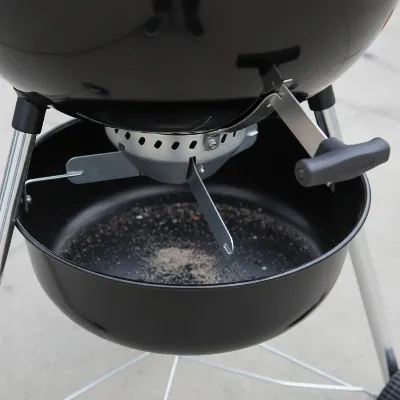 A close-up view of the Weber Original Kettle's One-Touch cleaning system, showing the ash catcher and damper lever, realistic style.